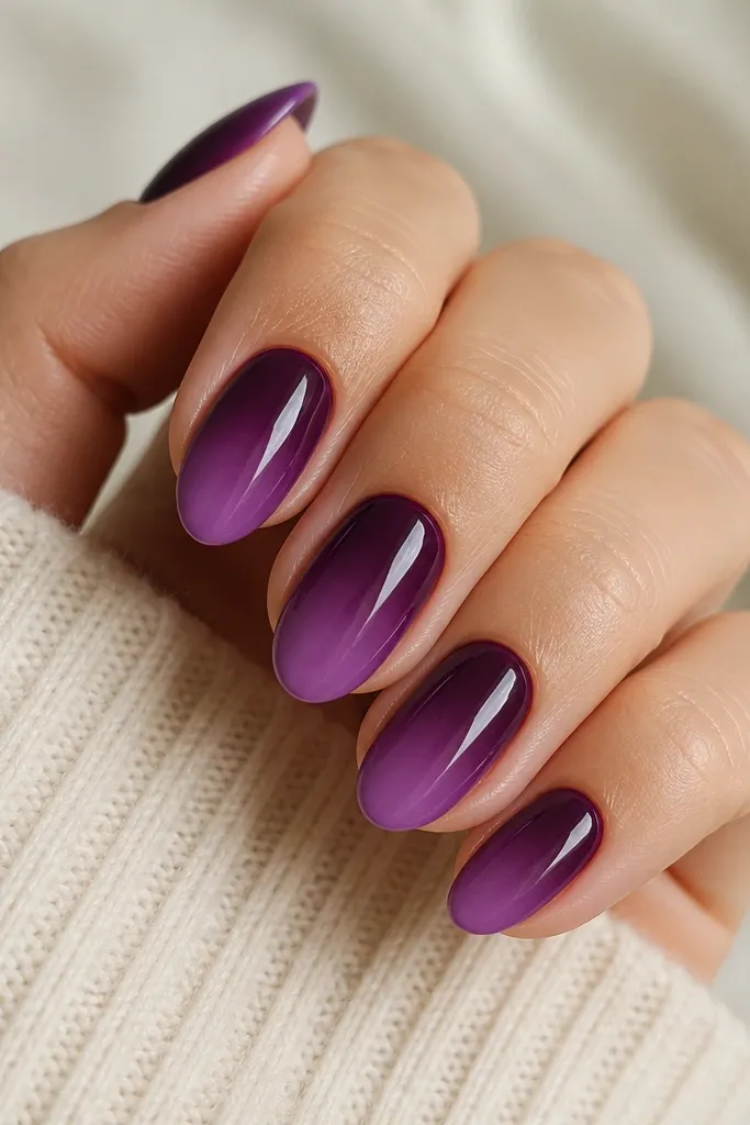 Short almond nails. The base is a deep plum near the cuticle fading into a lighter grape toward the tips. Glossy top coat makes the gradient look smooth, with a clean cuticle line.