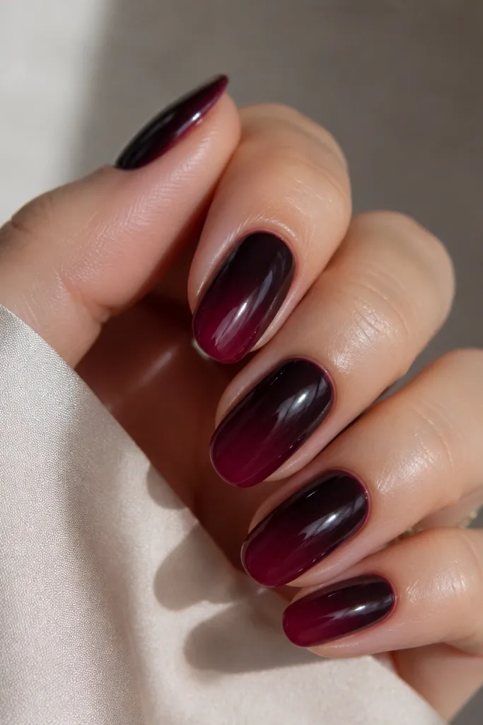 Medium-length oval nails. Dark wine-purple near the cuticle fades into a slightly lighter burgundy grape at the tips. The finish is high-gloss and looks like a salon gel gradient.