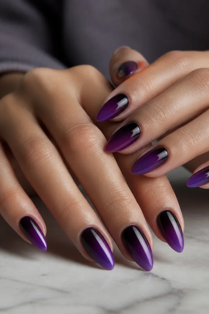 Short stiletto nails. Almost-black purple sits at the cuticle, fading into a classic deep purple, then into a lighter grape at the tips. The cuticle area looks darker than the rest.