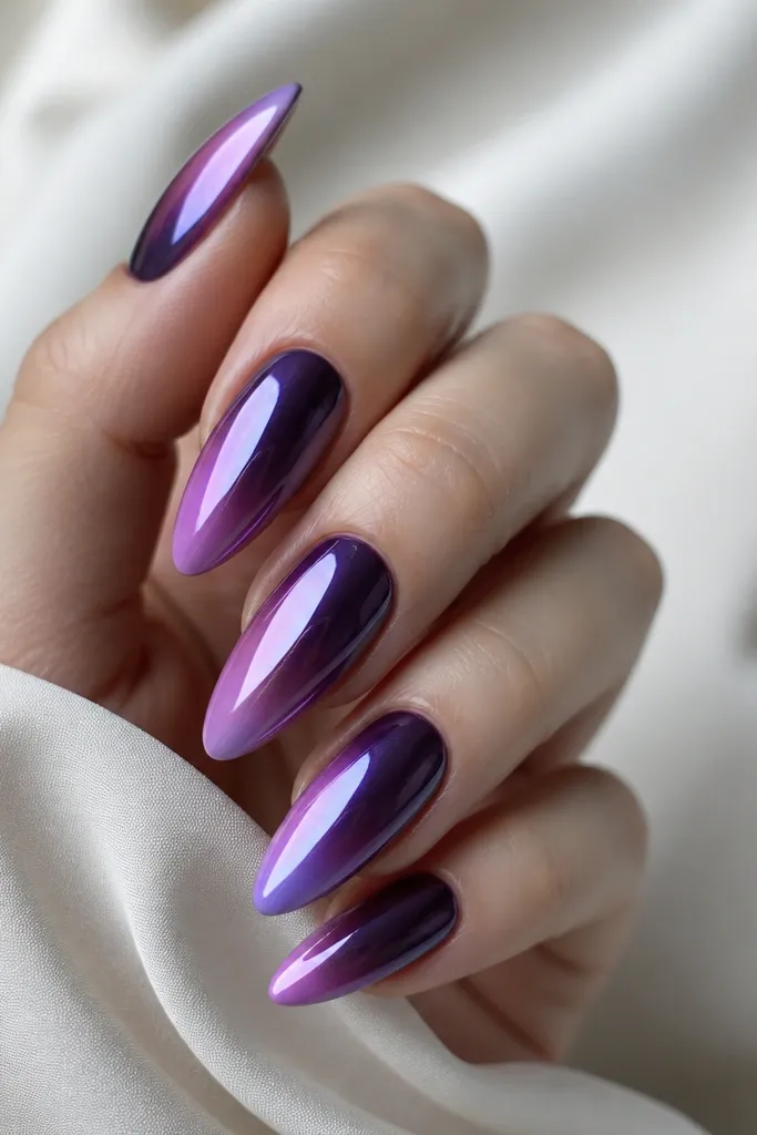 Long almond nails. Dark purple ombre fades into a lighter purple at the tips. The top portion has a purple chrome powder effect that looks mirror-like, especially near the tips.