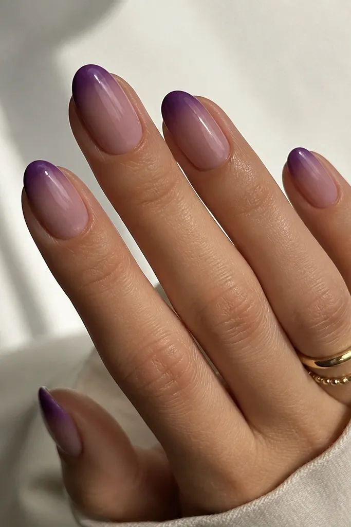 Medium oval nails. The base is a sheer plum-tinted nude. The ombre effect is at the tips, fading from dark purple at the very edge into lighter purple near the center.