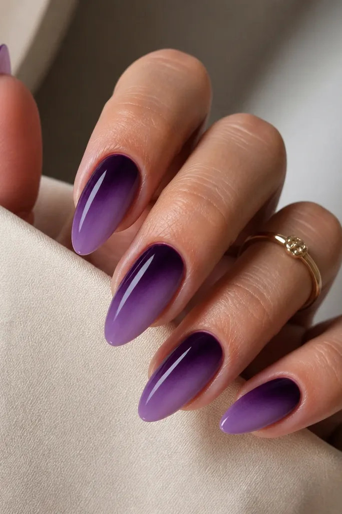 Long almond nails. Dark purple fades diagonally from one side near the cuticle down to the opposite side near the tips, creating a diagonal gradient. Glossy finish.