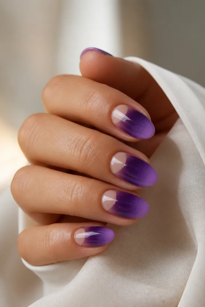 Short almond nails. The cuticle area is left bare or sheer nude, shaped like a half-moon. The ombre starts below it with dark purple fading into lighter grape toward the tips.
