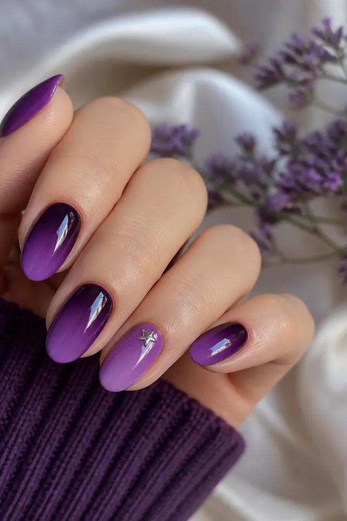 Medium oval nails. Dark purple ombre fades to lighter grape. One ring finger has a tiny silver star charm placed near the cuticle, with glossy top coat around it.