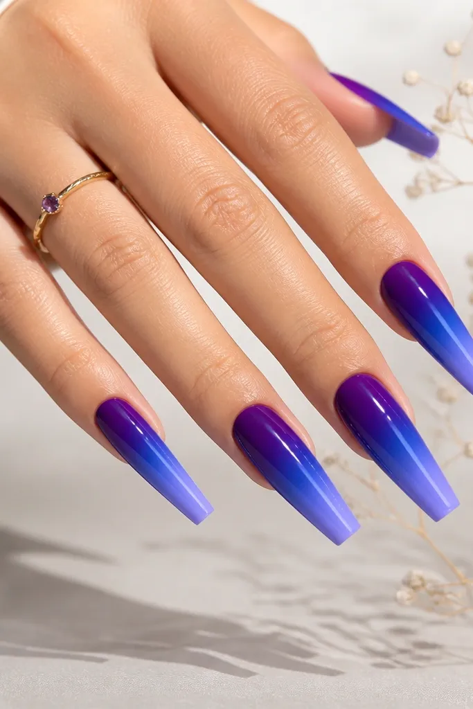 Long coffin nails. The gradient starts with deep purple at the cuticle, then blends into indigo blue mid-nail, and ends in a lighter periwinkle-purple at the tips. Glossy finish.