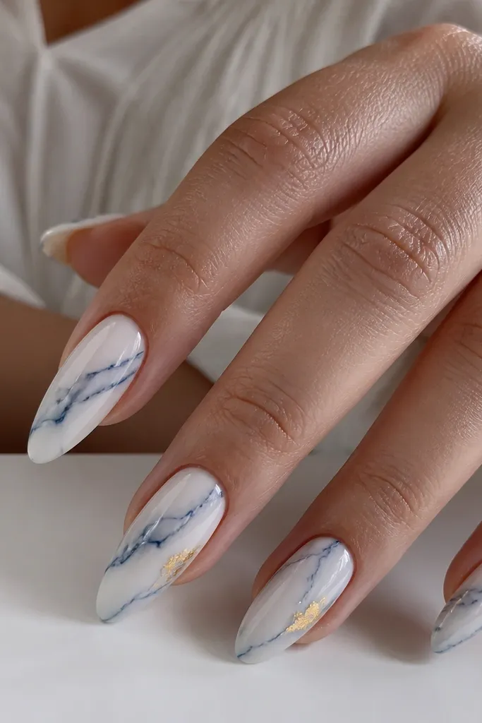 Long almond nails with a classic white base. Blue veins sweep diagonally like marble, with irregular thin lines. A small gold leaf fleck sits near the center of two nails.