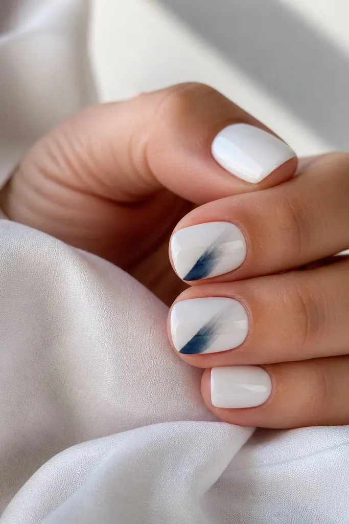 Short square nails in icy white. On two nails, a diagonal navy brushstroke sits near the sidewall, semi-transparent at the edges. The nails are glossy and clean.