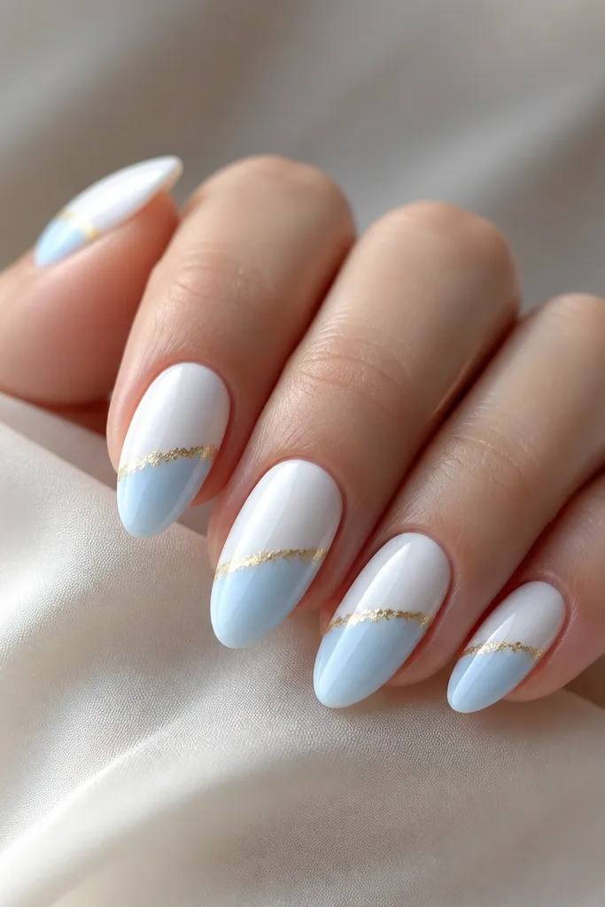 Medium almond nails split at midline. The bottom half fades from white into light blue, the top is classic white. Gold foil is placed in the lower corner where the colors meet.