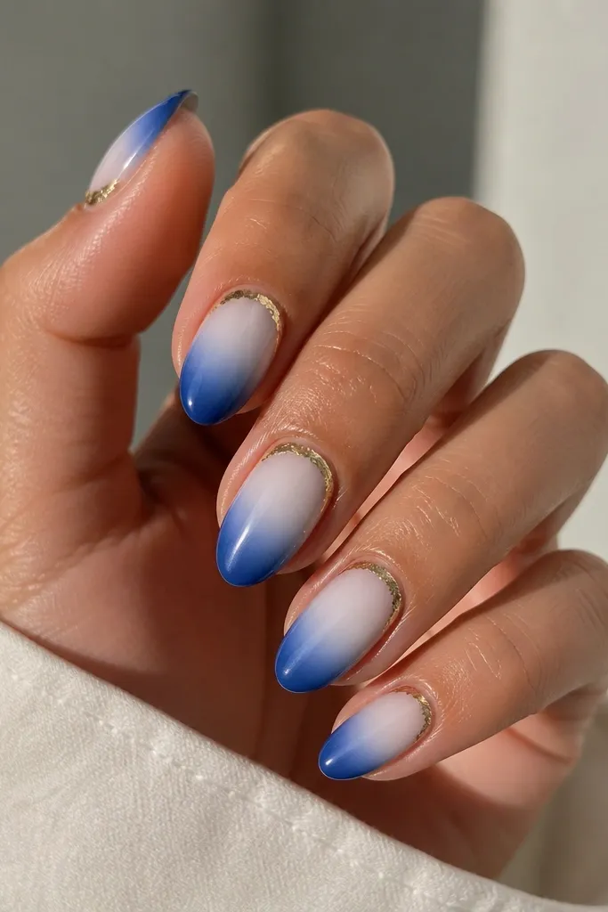 Medium almond nails. The tips fade from classic white into a deeper blue. Around the cuticle on each nail is a thin gold foil arc like a halo.