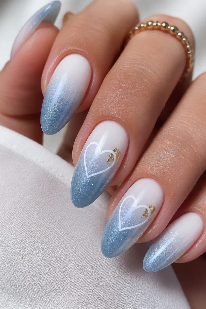 Gradient nails where the bottom starts classic white and fades into a shimmering blue. On two nails, a thin white heart outline is drawn in the center using glossy gel, with no fill. Gold foil flecks sit near the heart corners.