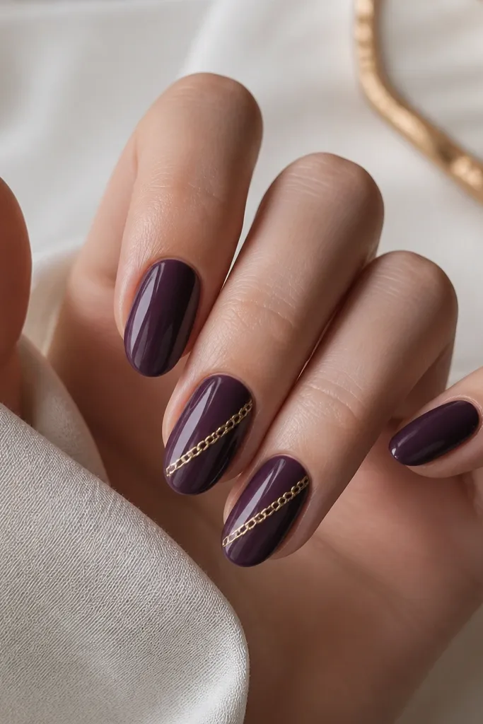 Glossy dark purple nails with thin gold chain-link lines running diagonally across two nails, like delicate jewelry.