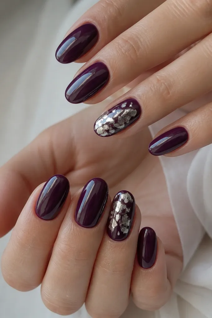 Deep purple nails with two accent nails. The accents have irregular silver foil shards scattered from mid-nail to tip, with sharp reflective edges.