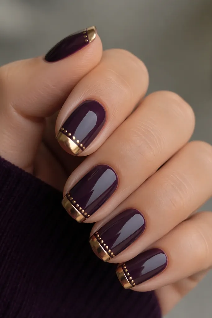 Squoval nails with dark purple glossy base and a gold half-tip. Tiny gold studs sit in a straight line near the tip curve.
