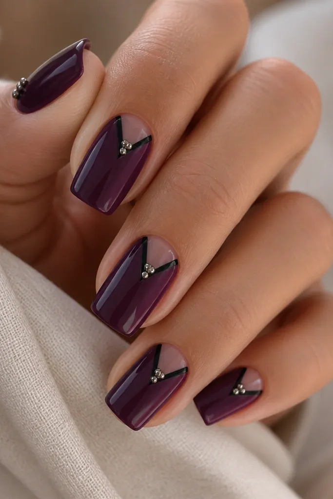 Square nails with a deep plum base and a thin black V-shape at the center of each nail. The V points toward the cuticle, and a few tiny silver micro studs sit at the inner point of the V. Glossy finish, sharp V lines, tidy cuticles.