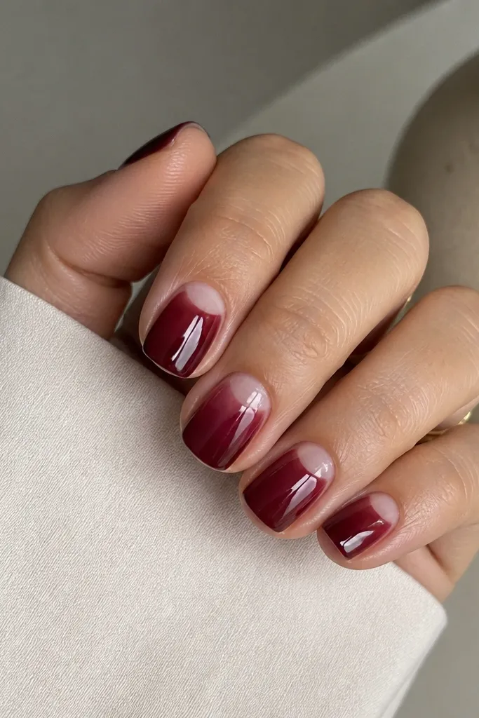 Short square nails in a sheer burgundy jelly color. The cuticle area is left clear in a clean half-moon shape, and the nails are glossy with a smooth gradient-like look.