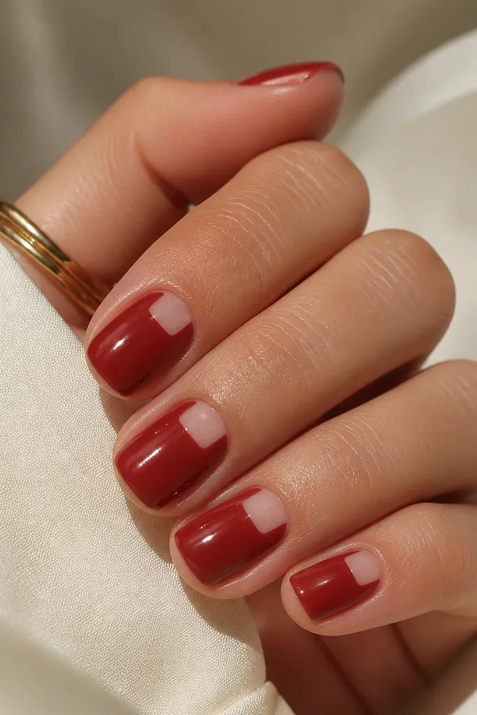 Short square nails painted spiced red. On each nail, there is a nude window in the center near the cuticle that looks like a rectangular negative space panel. Glossy finish.