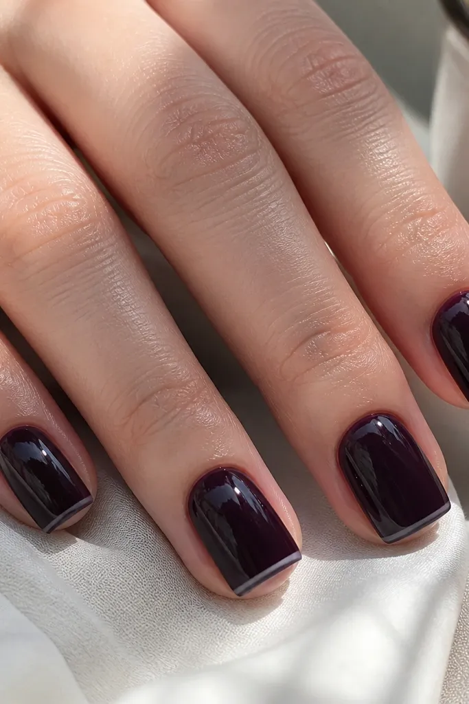 A set of short-square acrylic nails. The base is a near-black plum. The free edge is a super thin micro-French line in the same plum, with the very tip left clear and glossy. No glitter, just crisp contrast and a mirror shine.