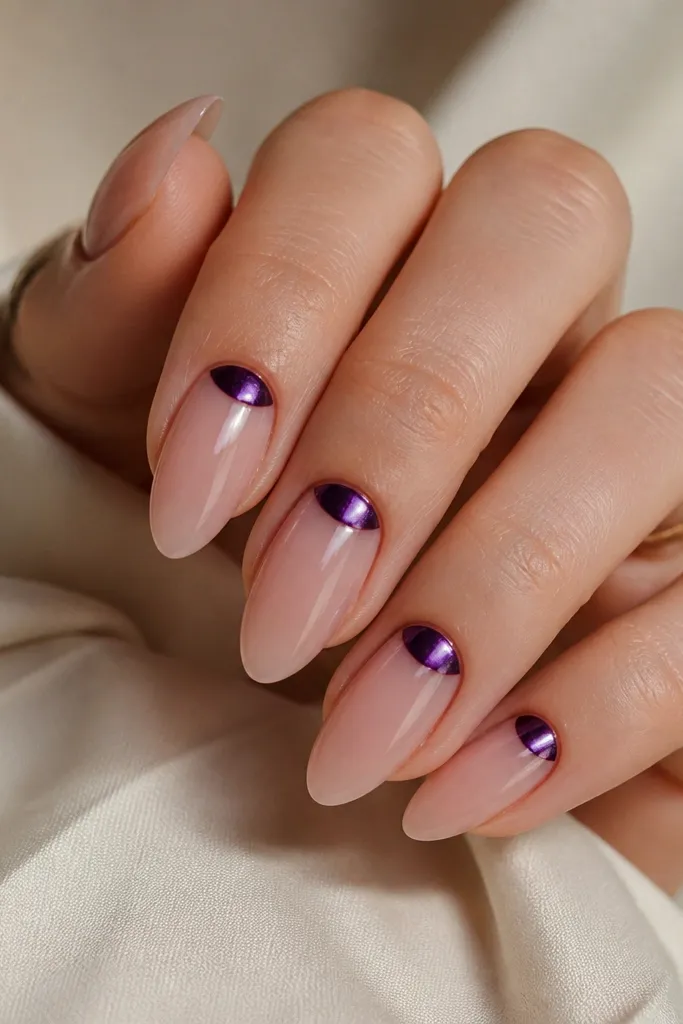 Almond nails with a sheer nude base. The cuticle area has a dark purple chrome half-moon shape that looks metallic and reflective. The rest of the nail is nude and glossy.