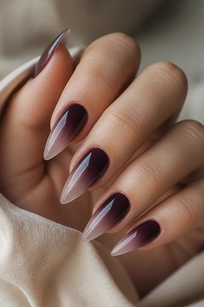 Medium-length stiletto nails with a dark plum ombré. The deepest purple is near the cuticle, fading smoothly to a nearly clear tip. The gradient looks airbrushed and super smooth.