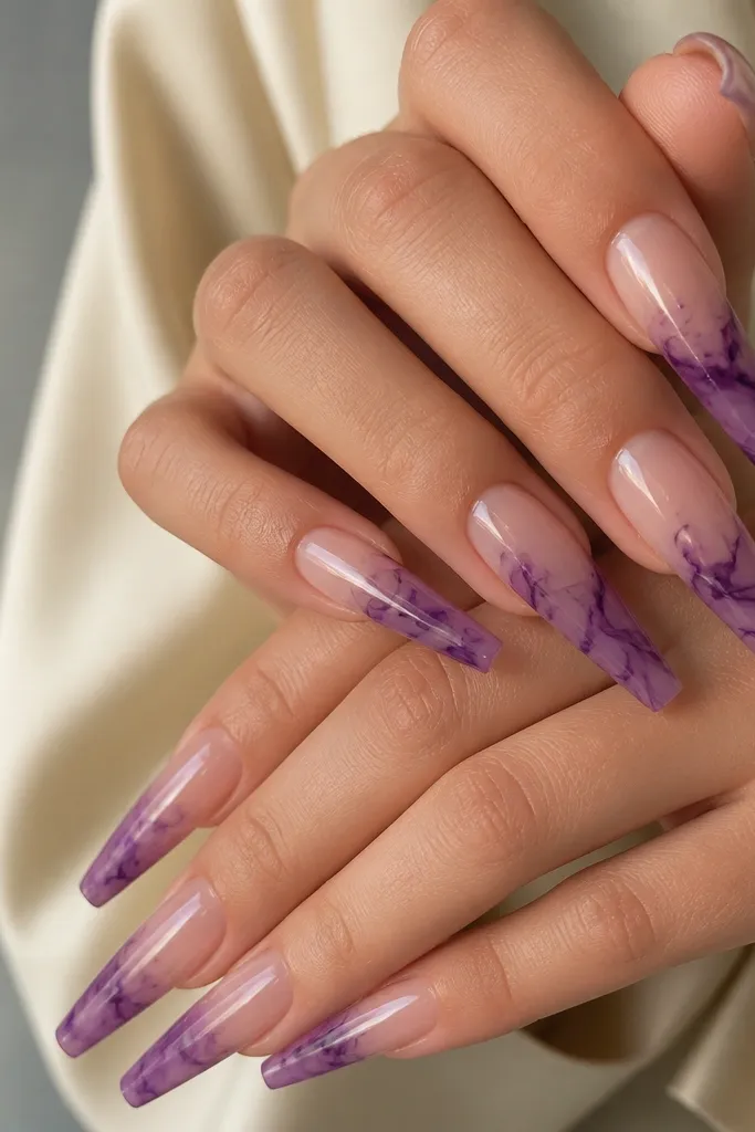 Long coffin nails with a clear or jelly nude base. The free edges have dark purple marble veining, like ink spreading in water. The veins are thin and layered, with a glossy finish.