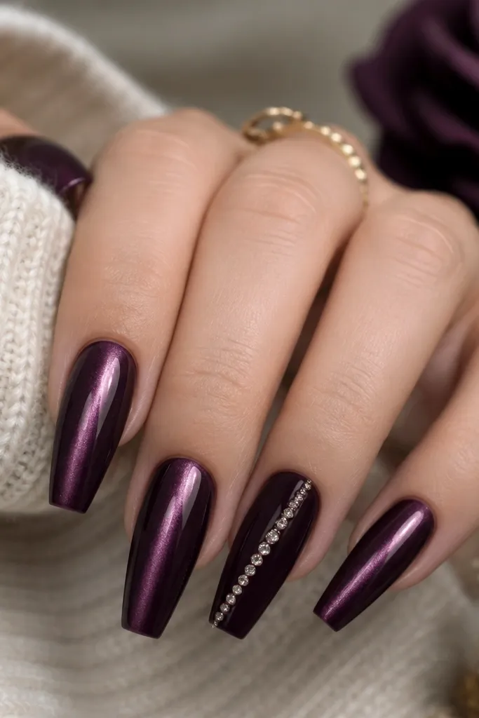 Medium-length coffin nails. Most nails have a plum cat-eye stripe that runs vertically down the center, with a glossy magnetic finish. One accent nail has a full dark purple base with a single diagonal line of tiny rhinestones.