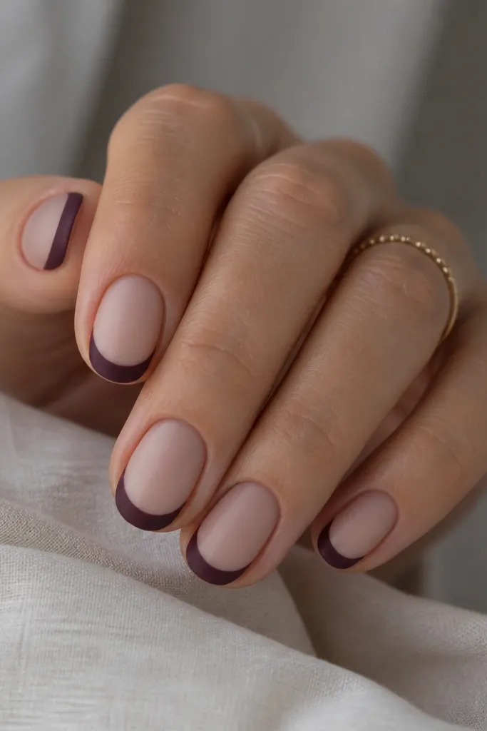 Short oval nails with a nude base. The tips are a velvet dark purple French line, slightly wider than micro-French, with a soft matte texture. The rest of the nail looks satin-like.