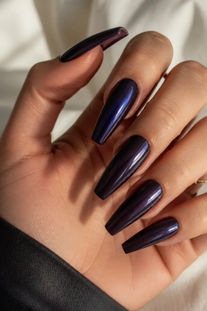 Long coffin nails painted a near-black deep violet. The surface is a full mirror chrome with sharp reflective highlights, especially on the center of each nail.