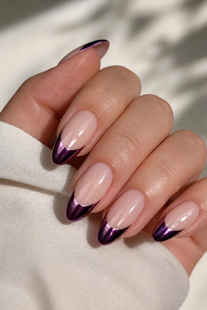 Almond nails with nude base at the cuticle and deep purple French tips. The tips are mirror chrome, while a thin strip of nude stays visible between cuticle and purple.