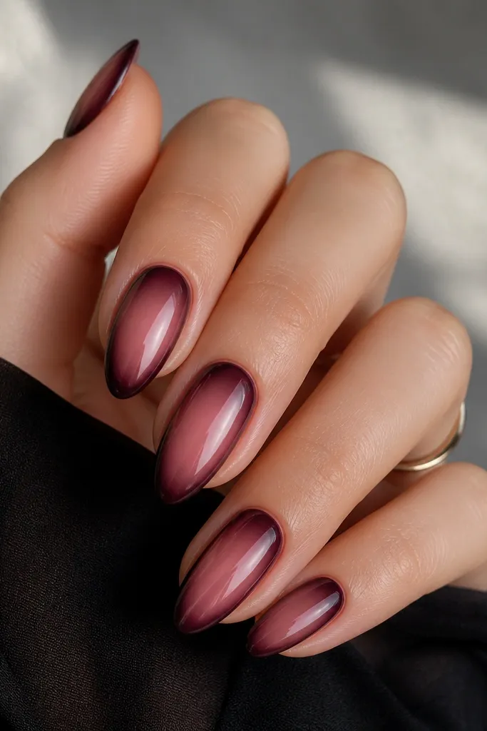 Almond nails with a smoky rose-pink ombré that fades into a darker edge. Around the outer sidewalls and tip, there's a thin blackened plum outline. The overall look is glossy and moody.