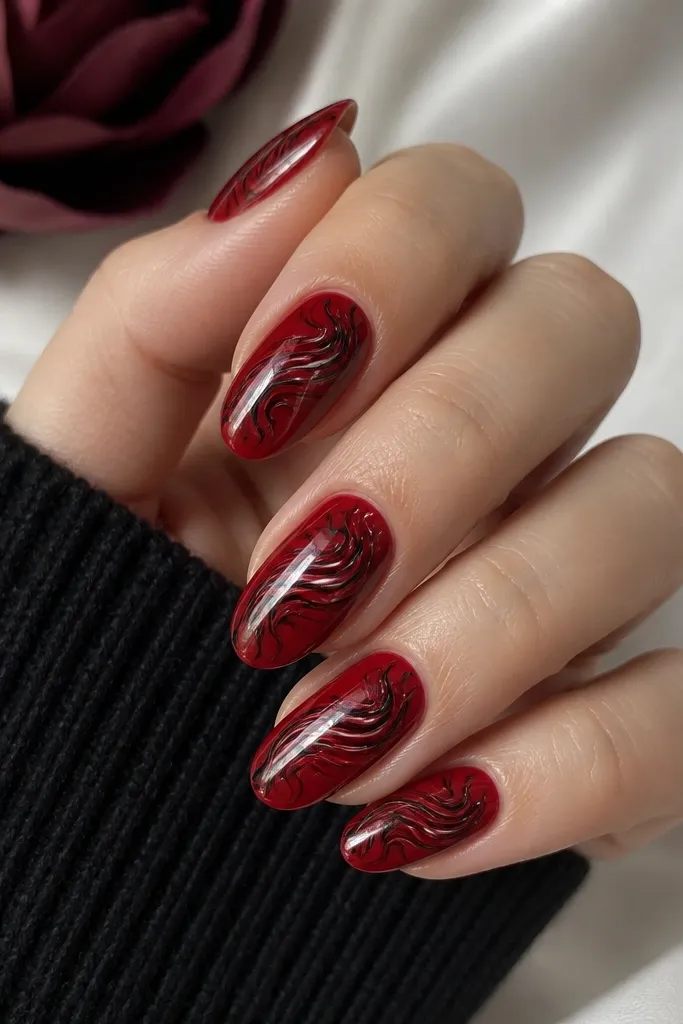 Medium oval nails with a deep red creme base. Each nail has black marble swirls that curl from the center and taper outward, with thin wispy white highlights in places.