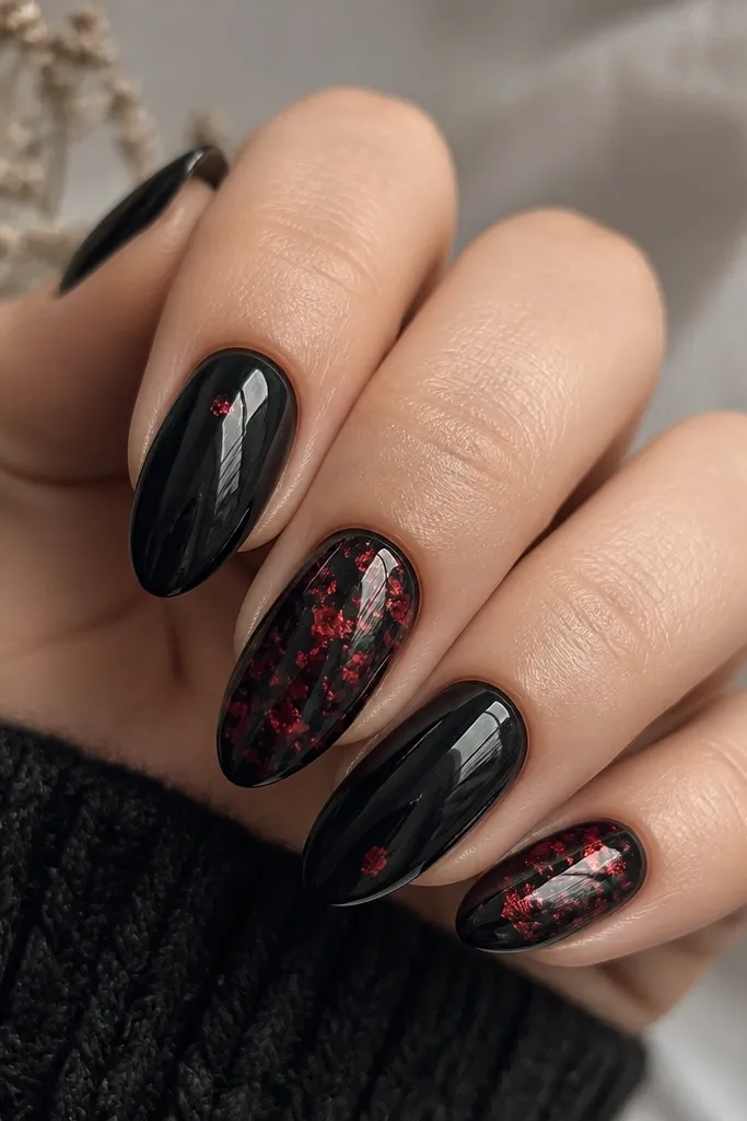 Medium almond nails with a deep glossy black base. Random red foil flakes sit on two nails, leaving negative space around the edges, while the other nails are solid black with one tiny red fleck.