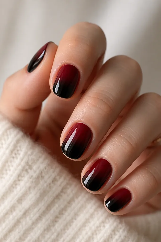 Short nails with a smooth gradient. The base is red near the cuticle, fading into black at the tip. The transition is soft, with a glossy finish.
