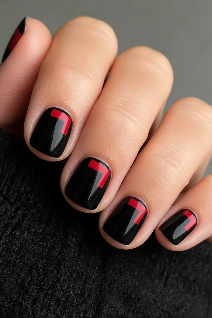 Short square nails painted glossy black. On each nail, a red L-shape sits in the upper corner near the cuticle, leaving most of the nail black. Thin black outline lines trace the red frame, and the rest stays clean and glossy.