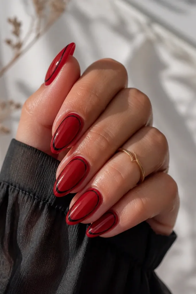 Medium-length almond nails with a glossy cherry-red base. A black outline traces the inner edge of the French area, leaving a clean red border near the cuticle. The black line is thin and crisp, almost like a frame, with a glossy top coat.