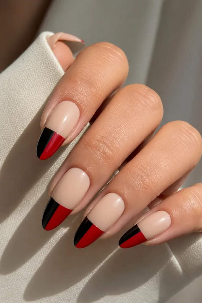 Long almond nails with a glossy nude base. The tips are split vertically down the center: left side is black, right side is red, meeting at a crisp line. The split line is straight and the top coat is glassy.