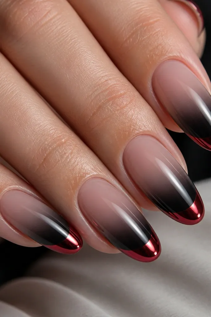 Close-up of a set of medium almond nails. The base is sheer nude with a smoky black French fade that looks airbrushed, starting mid-nail and softening toward the sides. The very tip is a glossy blood-red French line coated with high-shine chrome powder, reflecting light in sharp streaks. The black fade has a slightly smoky edge with no hard border, and the red tip is crisp and centered.