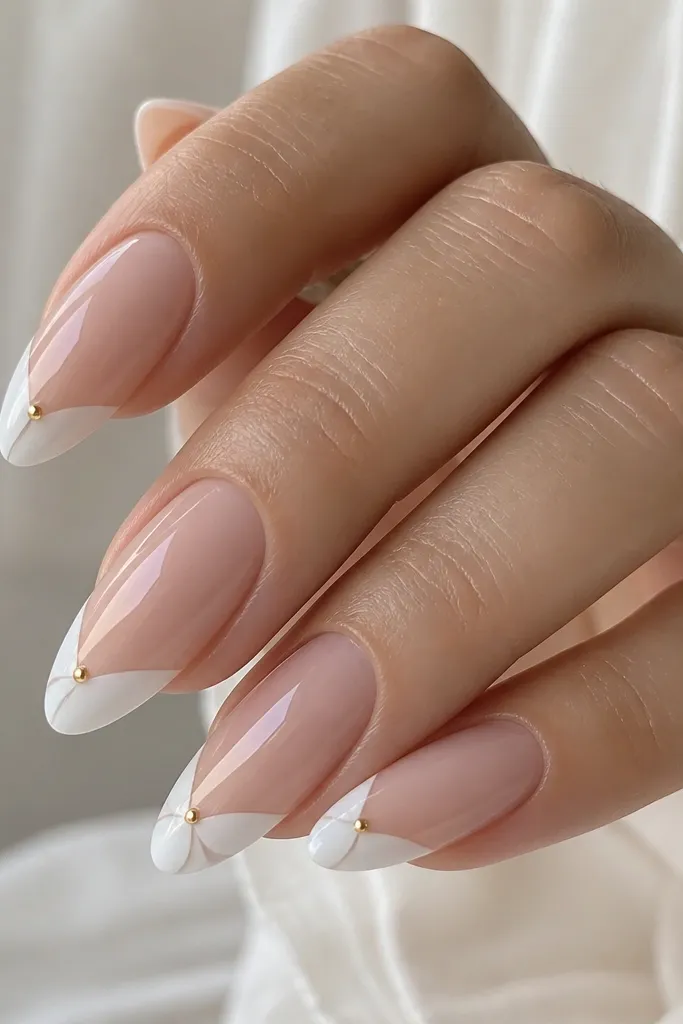 Almond nails with a sheer nude base. At the tip, there's a layered white bow shape made from two small curved panels. One small gold dot sits near the bow center. Glossy top coat, bow edges are sharp and symmetrical.