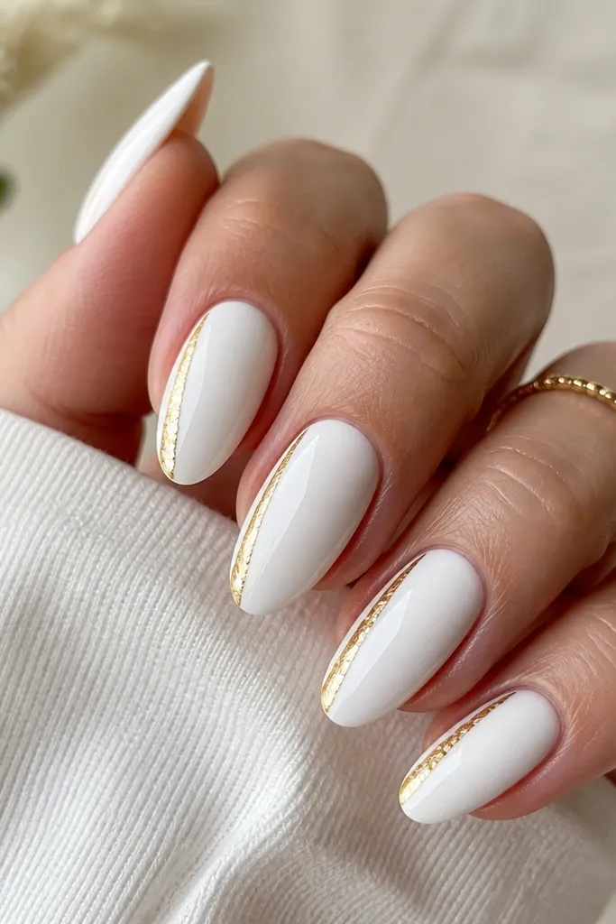 Almond nails with an opaque glossy white base. Along one side wall of each nail, there's a vertical strip of gold foil that runs from near the mid-nail to the tip. The other side stays plain white. Bright, reflective top coat.