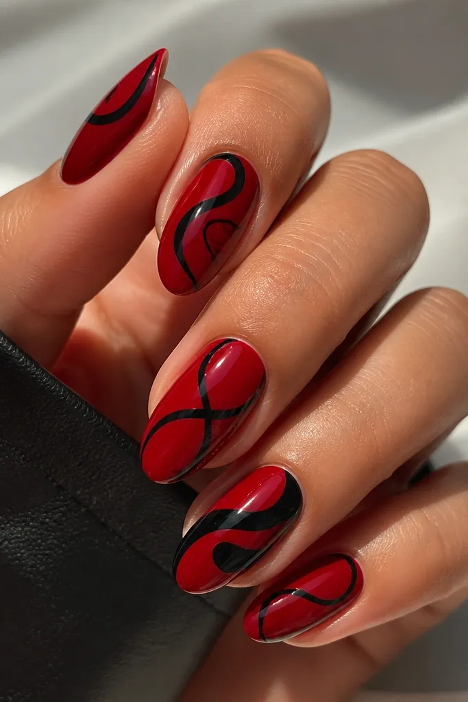 Base is a glossy cherry red on all nails. Over it, black swirls are painted leaving negative space curves of red. The swirls look like looping ribbons, with one nail having a thicker black swirl.