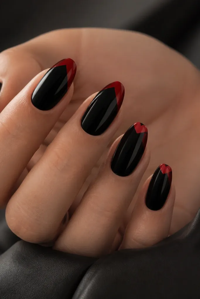 Glossy black nails with red chevron tips that look broken and angled. The red forms a V shape but the edges are slightly offset on each nail, creating a graffiti-like chevron effect.
