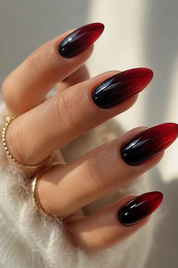 Glossy almond nails with a deep black base under a translucent red jelly ombre; the red looks like it's glowing through glass.