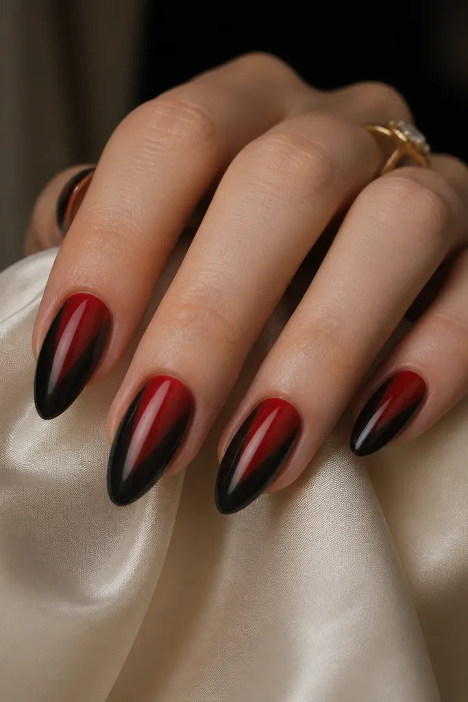 Almond nails with a V-shaped gradient: black fills the side edges and fades toward the center, where red brightens, creating a V pointing toward the cuticle.