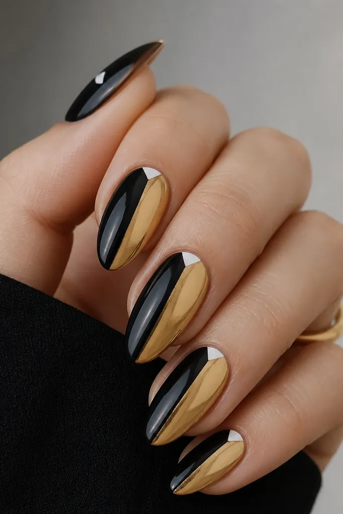 Almond nails split vertically: left half is glossy black, right half is gold chrome. At the top corner near the cuticle, a small white triangle points inward.