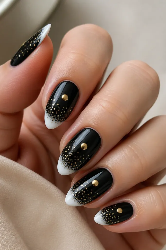 Short almond nails with a glossy white tip. The rest of the nail is black with small dot clusters that fade toward the tip. One large gold dot sits in the center of the nail.