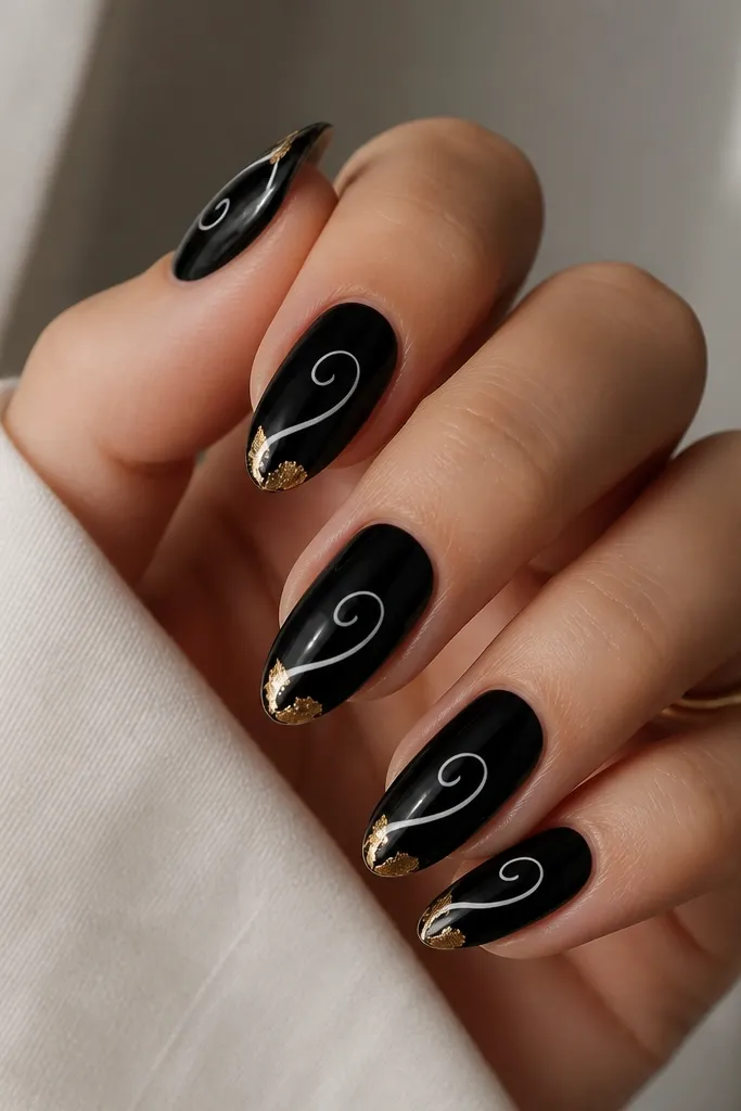Glossy black nails with a single flowing white swirl spiraling from mid-nail toward the tip. At the corners of the nail near the tip, small gold leaf pieces sit like flakes.