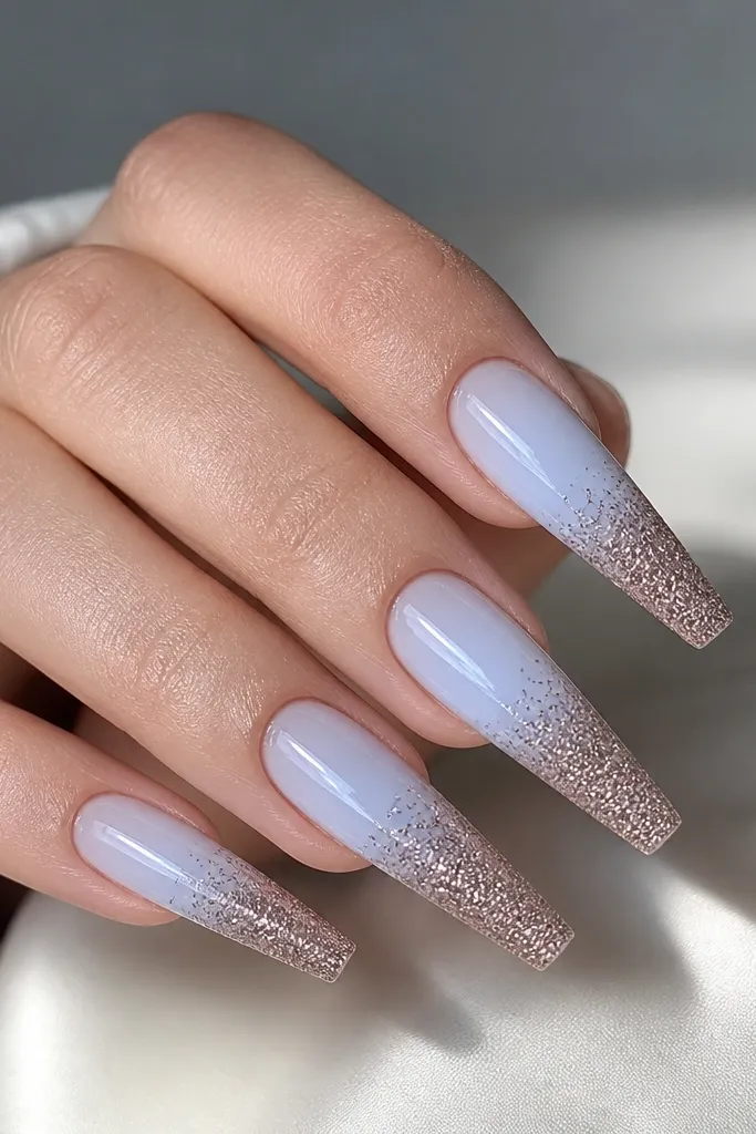 Long coffin nails. The base is sheer with a pale icy blue glow. The tips are covered in fine brown sugar glitter crystals in a gradient - denser at the tip, fading toward the middle. Everything is glossy except the crystal texture at the tips.