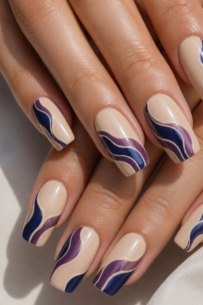 Long squoval nails with a creamy nude base. Swirls in deep blue and a touch of purple look like jam streaks. The swirls have glossy highlights and thin cream lines that separate the curves. No glitter, just smooth gel art.