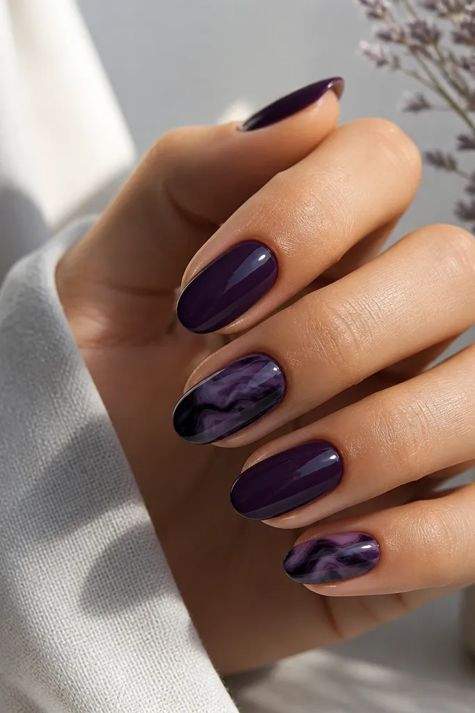 Most nails are solid dark purple; the accent nails have black and purple marble swipes like ink on water, with a glossy finish.