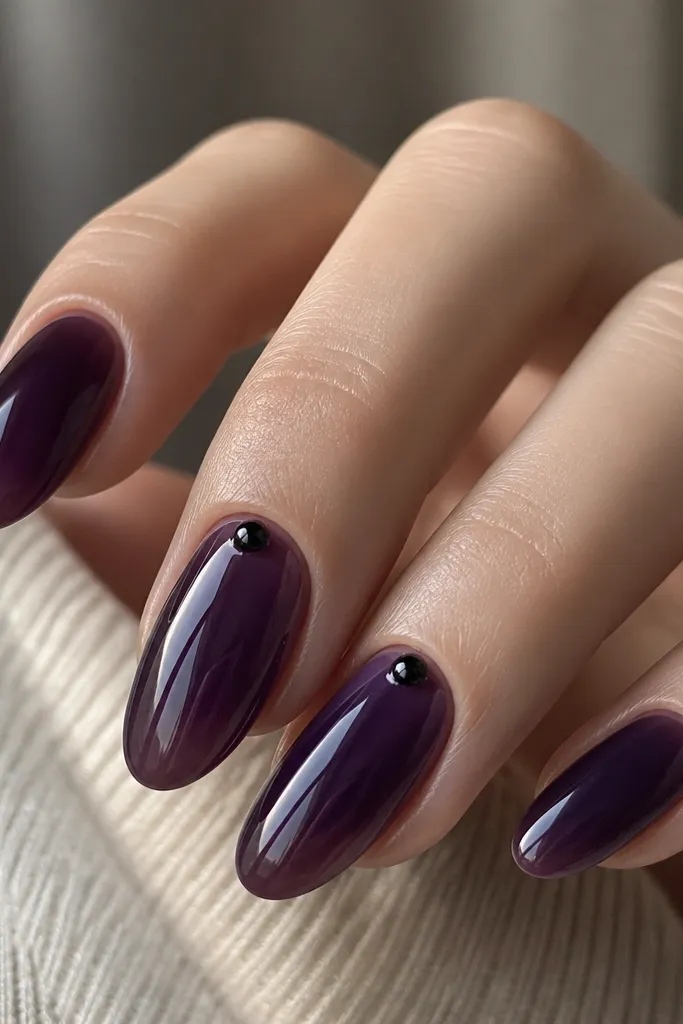 Dark purple jelly nails with a glossy, glassy look; small black studs sit near the cuticle on two nails, with clear shine around them.