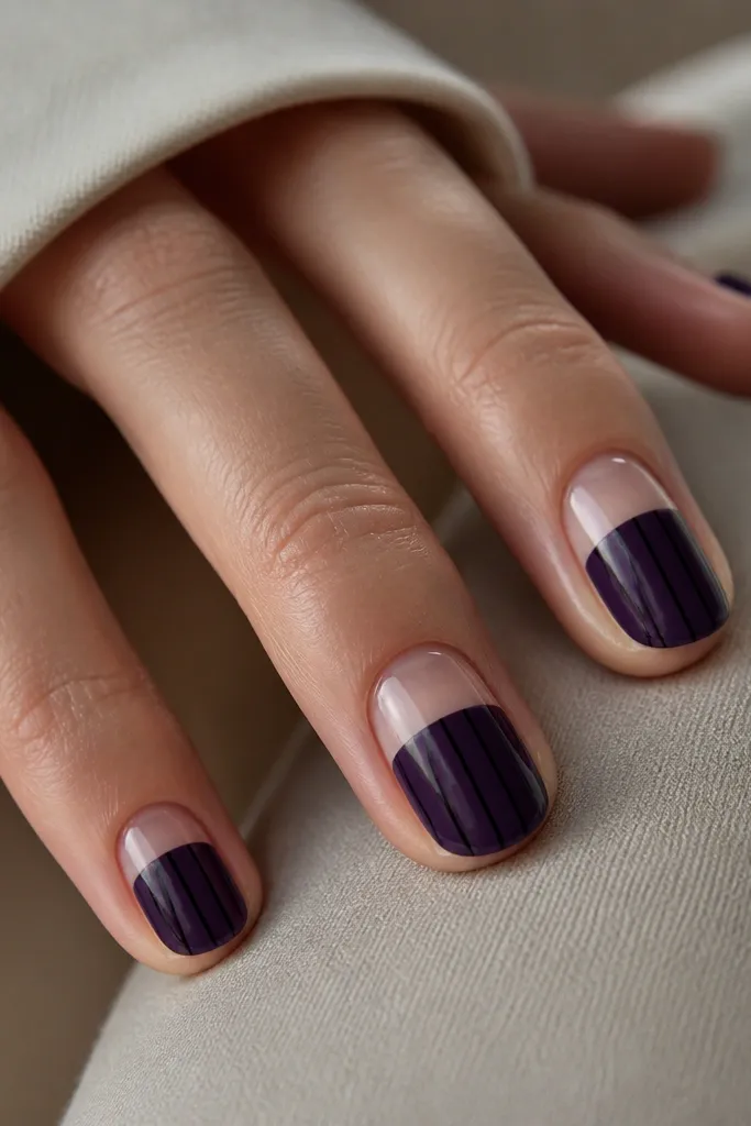 Half-negative nails where the bottom portion is dark purple and the top portion is clear; black vertical stripes run down the purple section, glossy.